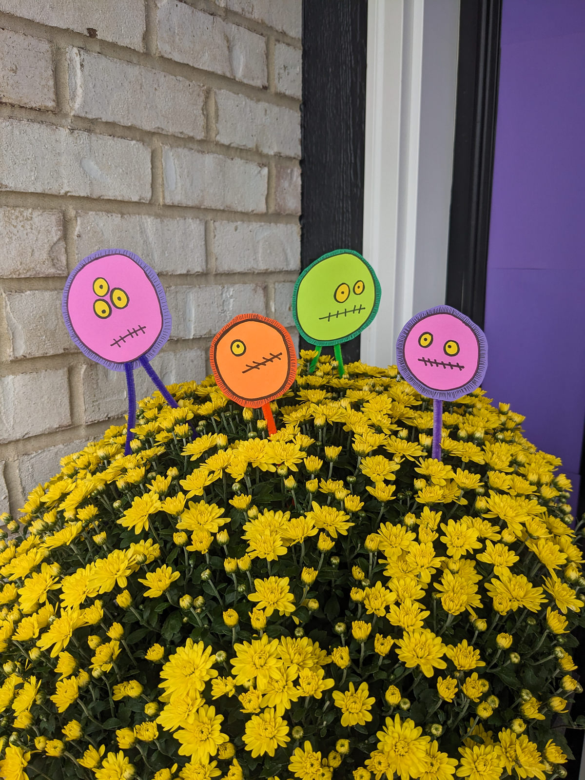 DIY Halloween floral picks with silly monster faces tucked into fall mums on a front porch