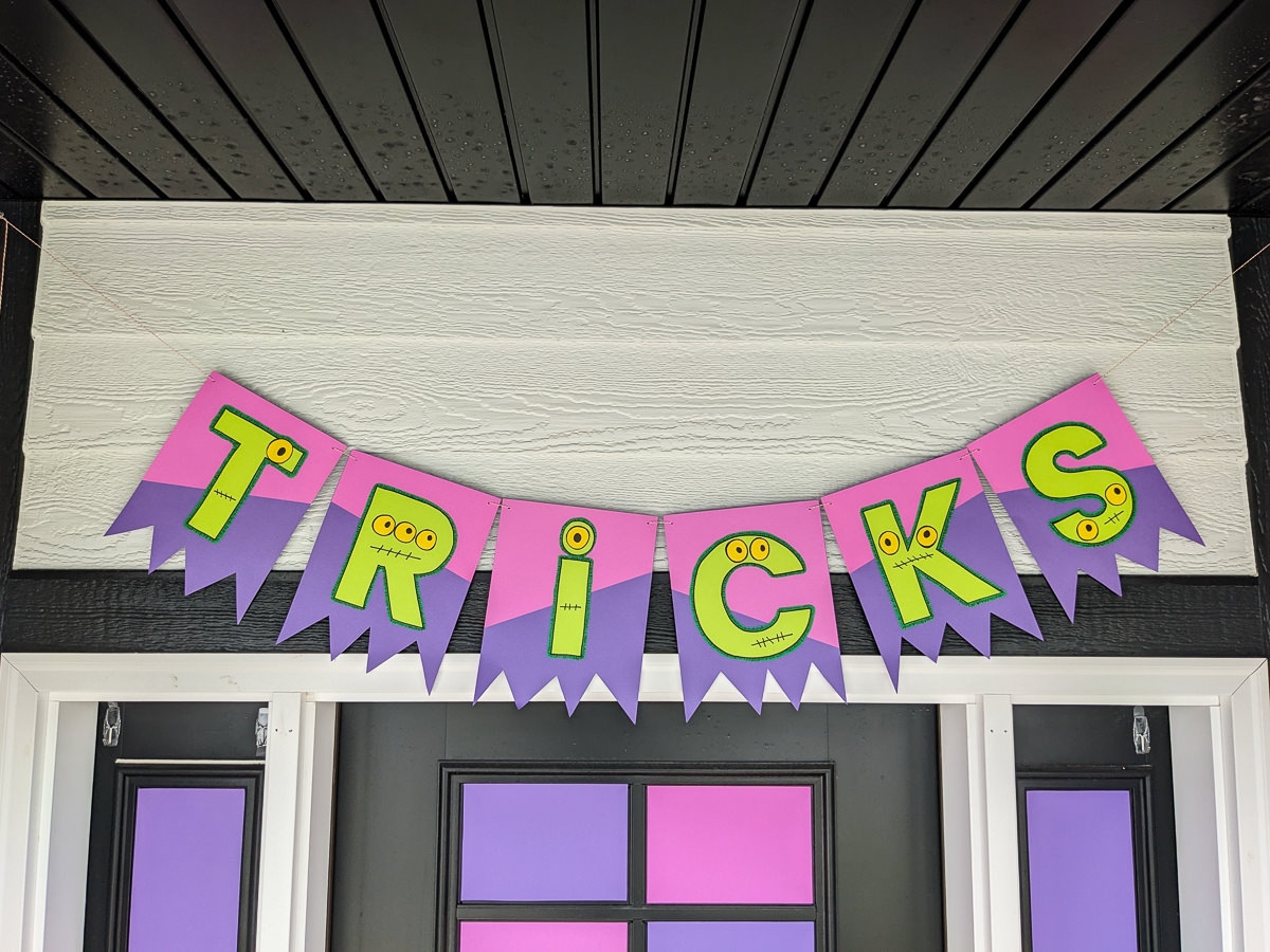 DIY Halloween banner that spells TRICKS with haunted monster eyes, stitched mouths, and shredded bunting from monster claws.