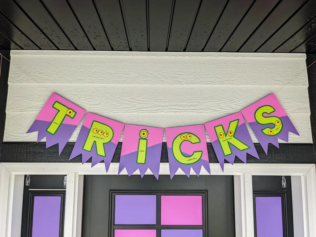 DIY Halloween banner that spells TRICKS with haunted monster eyes, stitched mouths, and shredded bunting from monster claws.