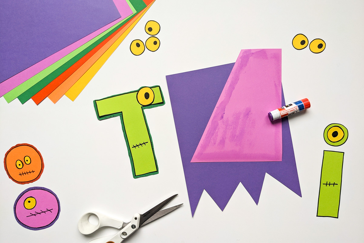 Gluing together a DIY Halloween banner craft that spells Tricks. Each letter looks like a monster with eyes and mouth. The bottom of each bunting looks like it's been shredded by monsters claws.