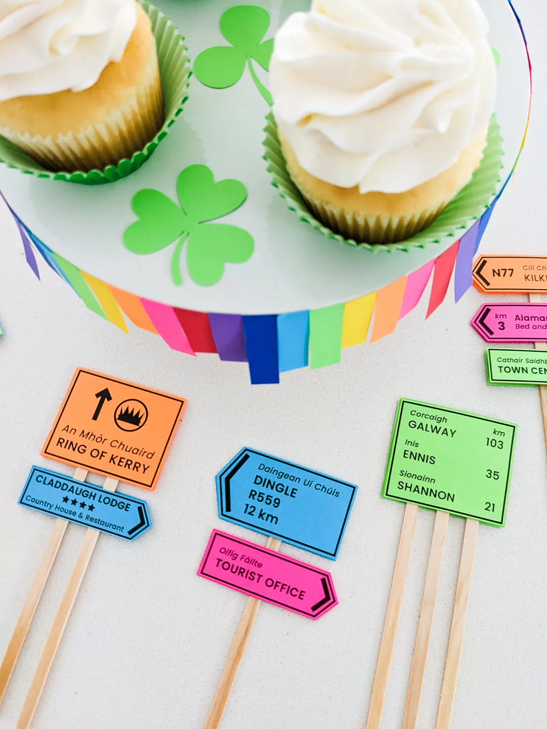 DIY Irish road signs cupcake toppers on a table next to cupcakes sitting on a rainbow cupcake stand