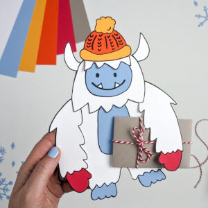 Paper Yeti wearing a winter hat and mittens and carrying a gift card wrapped as a brown paper package tied up with strings