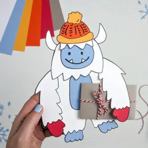 Paper Yeti wearing a winter hat and mittens and carrying a gift card wrapped as a brown paper package tied up with strings